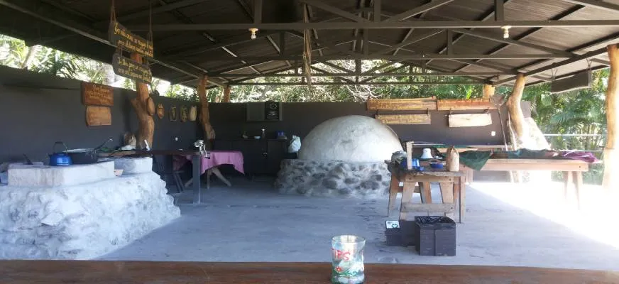 Rustic outdoor kitchen with stone oven, wooden tables and metal roof.