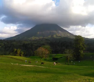 Arenal Volcano rises above a lush green landscape under a partly cloudy sky.