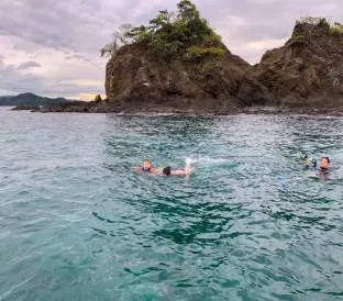 Two snorkelers swim in clear turquoise water near large rocky island formations.