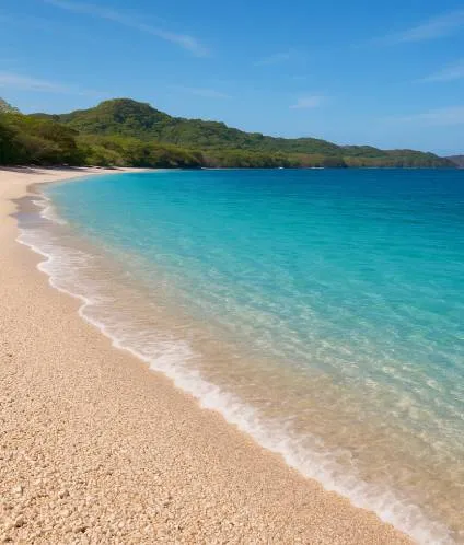 Light sand beach with turquoise waters under a clear sky and green hills in the background.