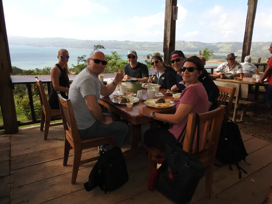 A group of tourists dine on an open-air terrace with a panoramic jungle view.