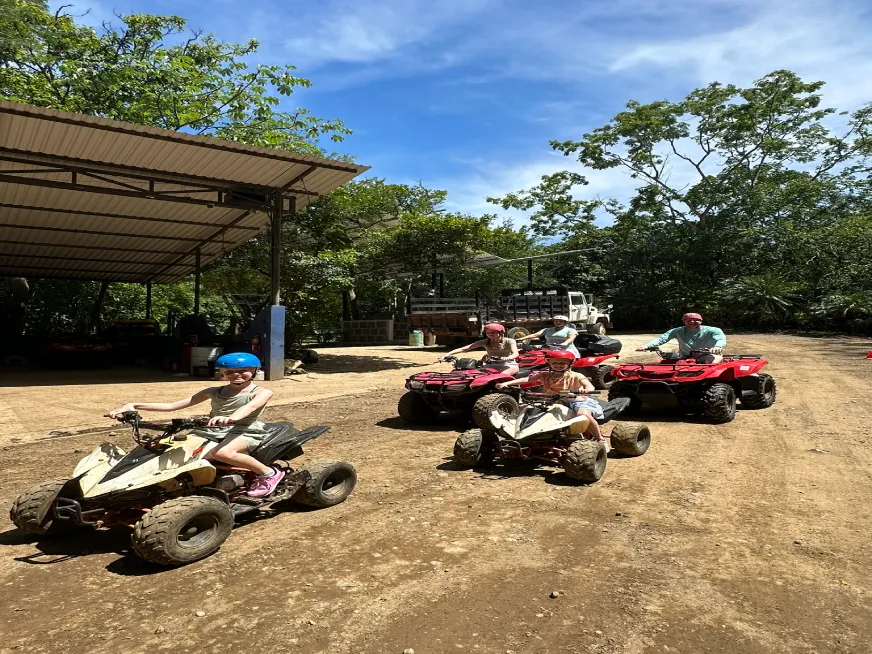 Group of people wearing helmets driving all-terrain vehicles on a wooded dirt road.