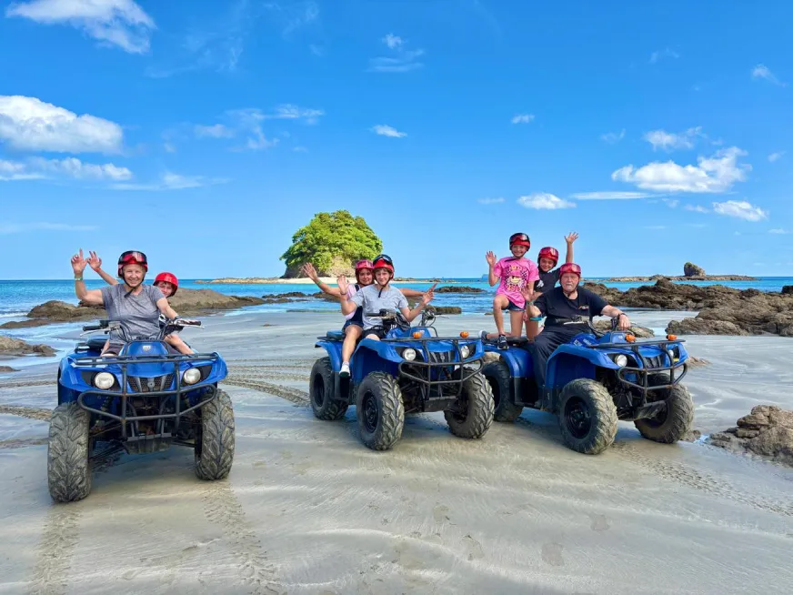 Group of people with red helmets on blue ATVs on a sunny beach with sea.