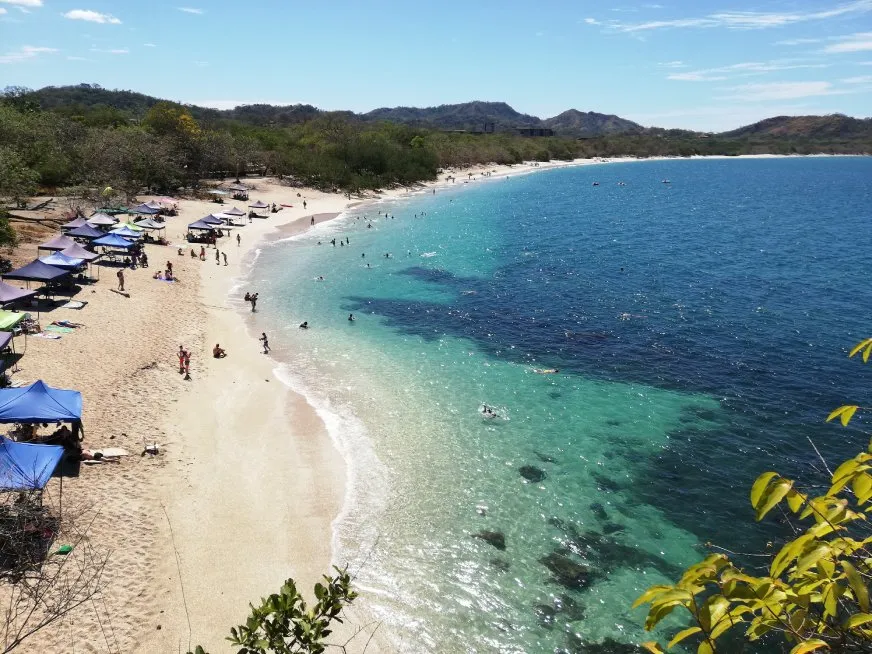 Aerial view of a tropical beach with blue tents, light sand and crystal clear waters under the sun.