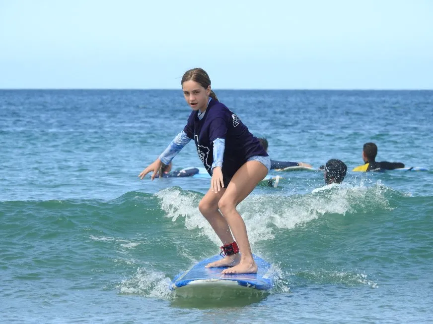 A young woman surfs on a blue board in the sea while other people practice in the background.