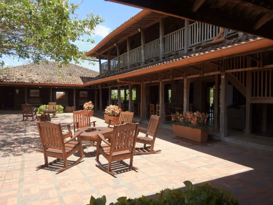Wooden rocking chairs arranged in a colonial courtyard with brick flooring and decorative plants.