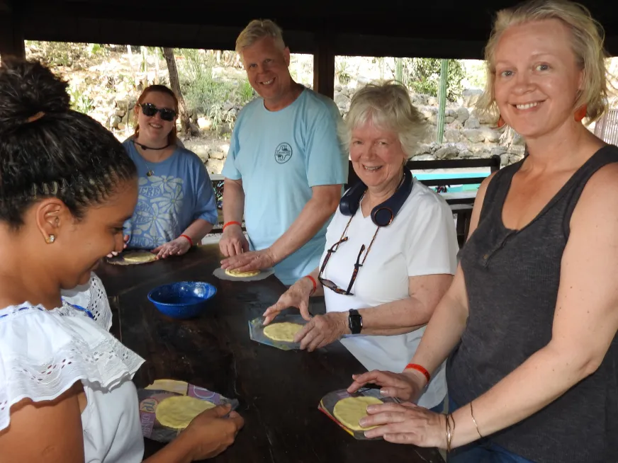 A group of smiling people prepare tortillas on a rustic wooden table.
