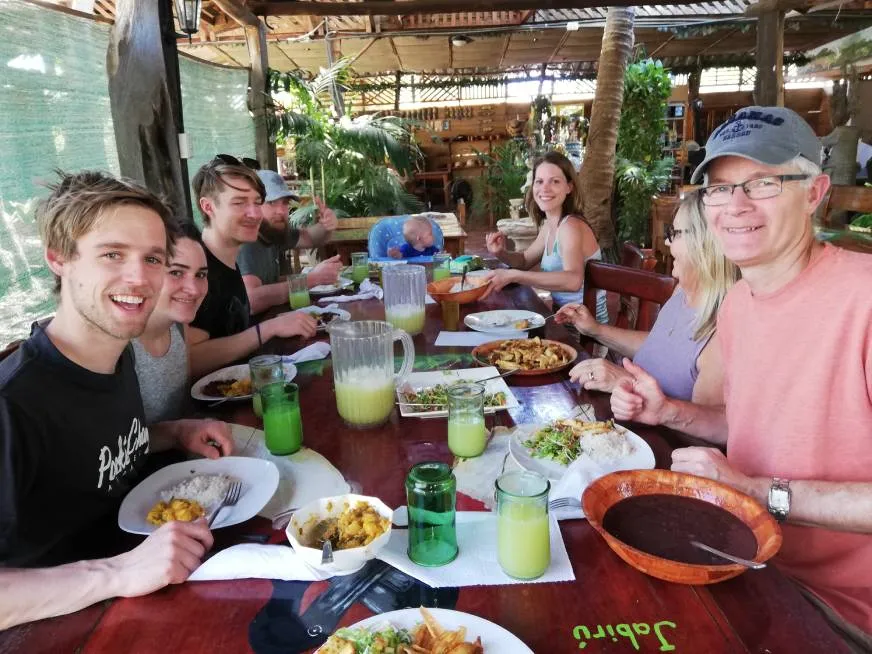 A group of people smile as they share a hearty meal at a rustic outdoor table.