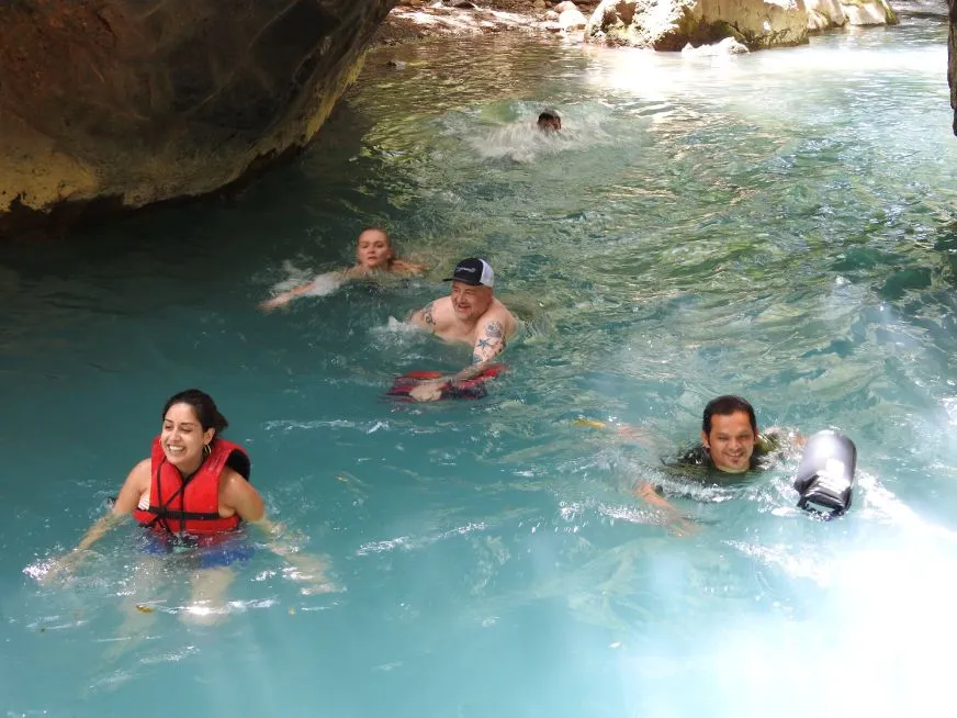 A group of people swim in a turquoise river near a rock formation.