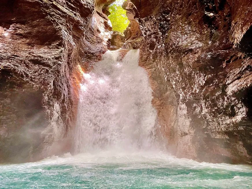 Waterfall that falls between dark rock walls into a turquoise pool.
