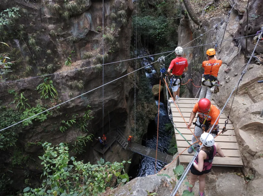 A person descends a zip line through a narrow rocky canyon passage in the jungle.