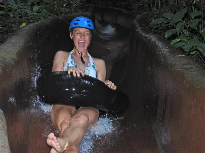 A smiling woman wearing a blue helmet floats through a dark cave on an inner tube.