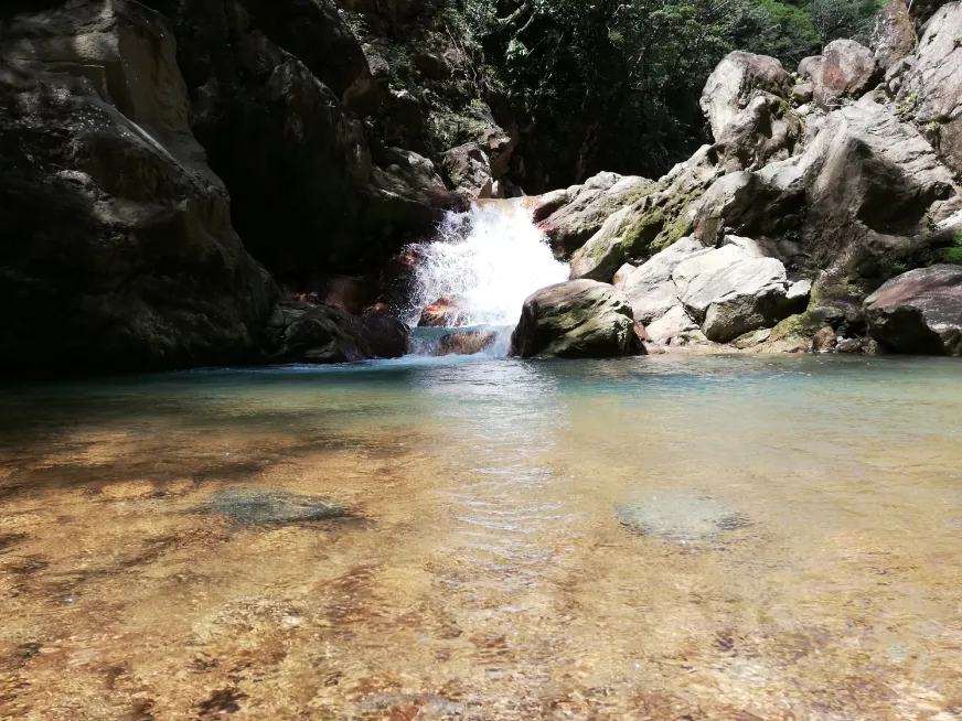 A clear turquoise river flows between large grey boulders in a rocky canyon.