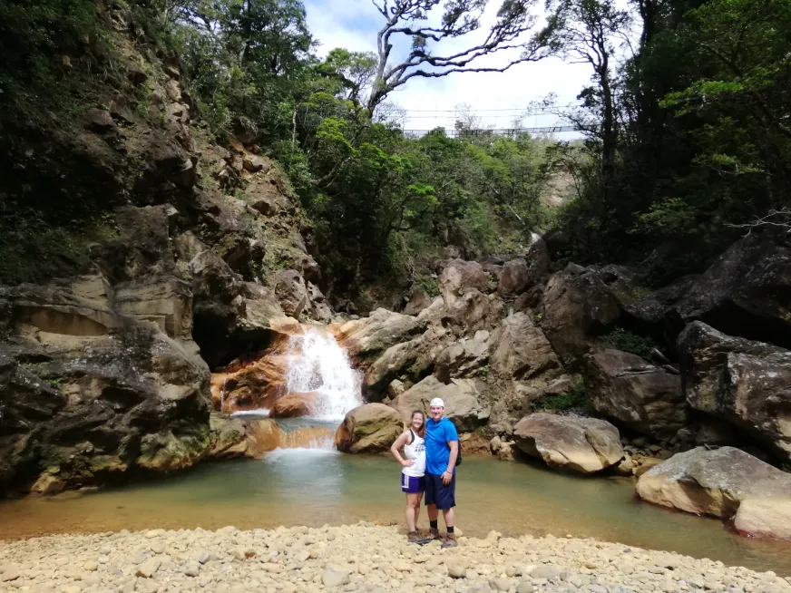 A hiker walks along a narrow trail beside a turquoise river flowing through a rocky gorge.