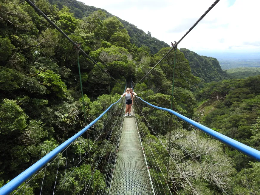 A person zip lines across a blue cable above a deep volcanic canyon with mountain views.