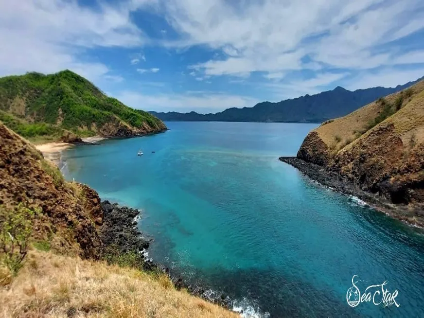 A vivid turquoise bay surrounded by green rocky islands under a clear blue sky.