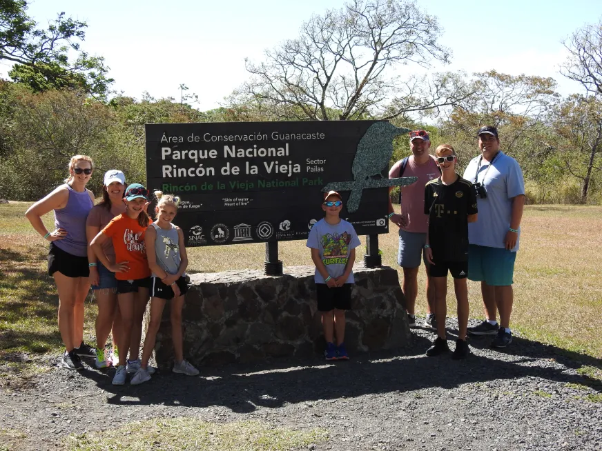 A group of tourists poses in front of the Rincon de la Vieja National Park entrance sign.