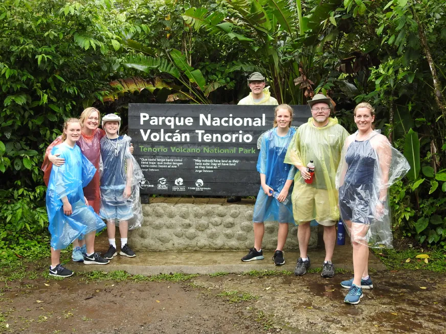 A group of tourists poses in front of the Parque Nacional Volcan Tenorio entrance sign.