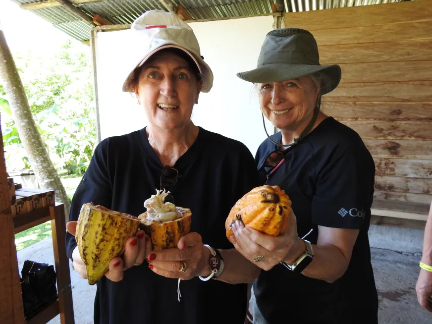 Two smiling tourists hold a freshly harvested cacao fruit during an eco tour outdoors.
