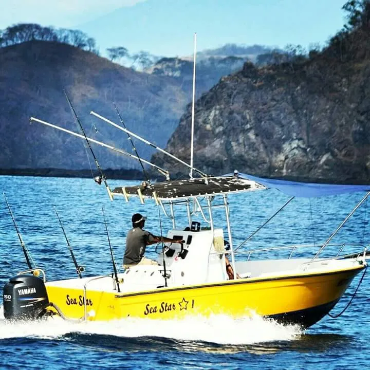 A yellow Sea Star I fishing boat sailing on the sea in front of rocky mountains.