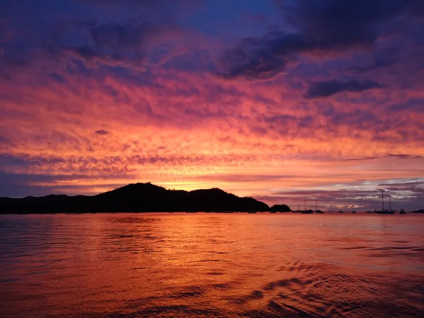 A dramatic purple and pink sunset sky reflects over a calm ocean with rocky island silhouettes.