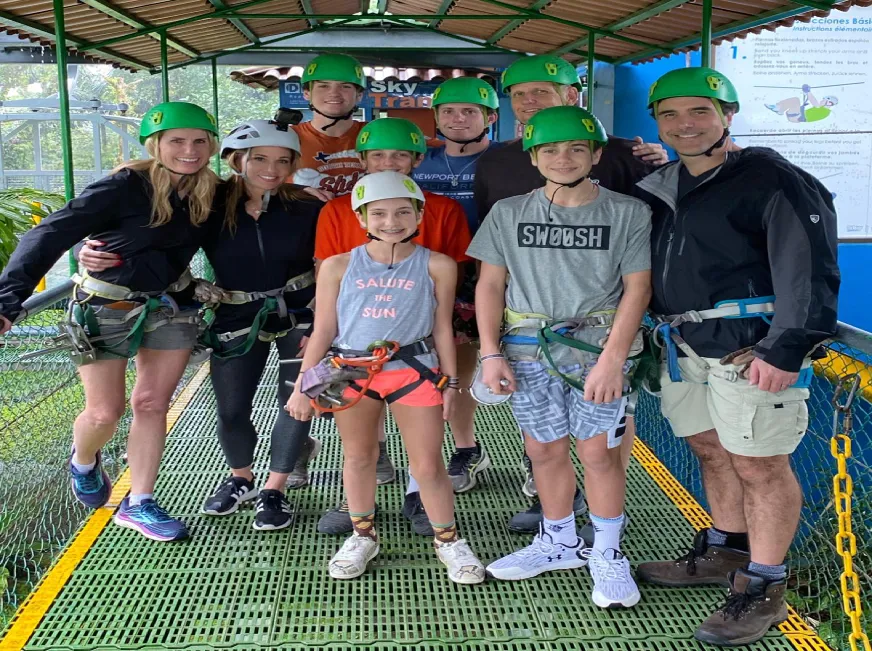 A group of smiling tourists poses together inside a green sky tram gondola in the rainforest.