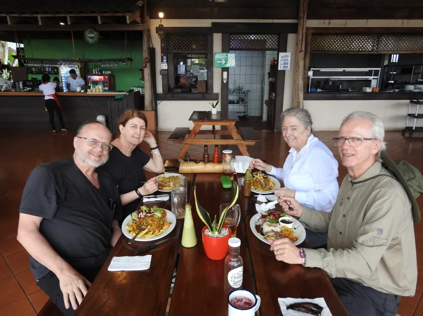A group of tourists enjoy a meal together at a table inside a rustic jungle restaurant.